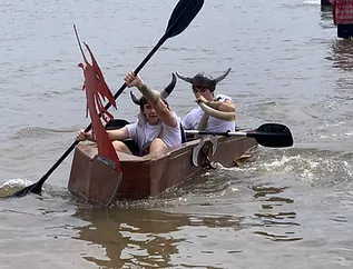 Two people paddling a cardboard boat decorated as a Viking ship